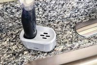 A closeup of an OXO dishwashing wand in a plastic holder next to a kitchen sink