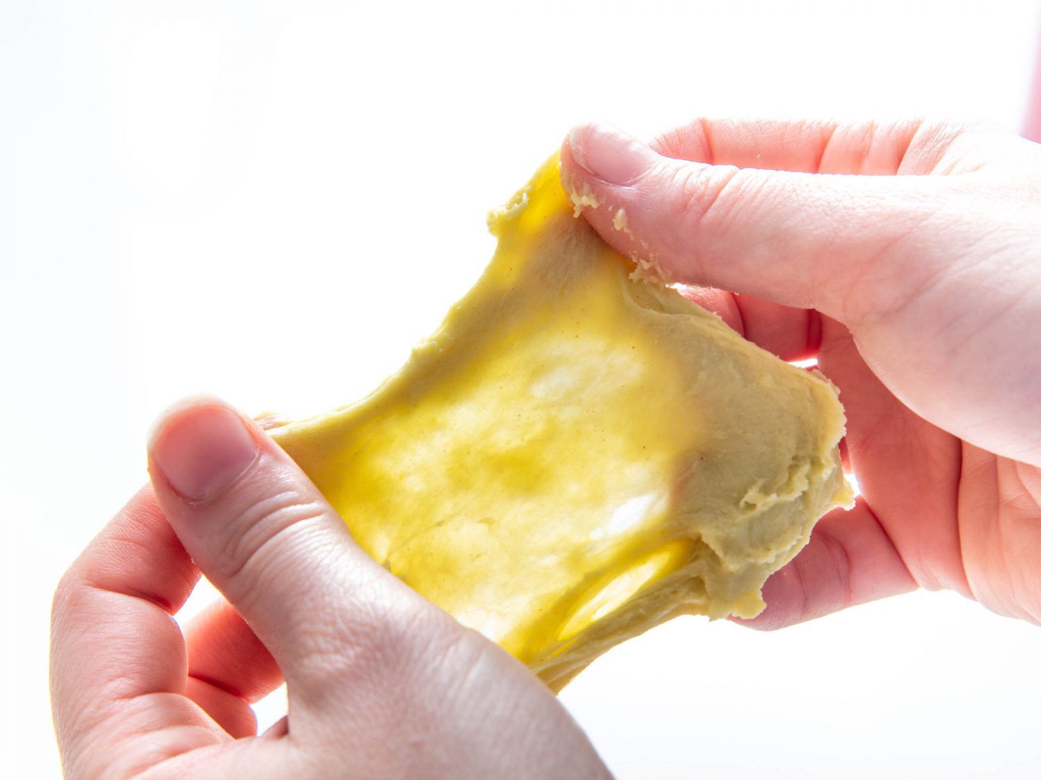Stretching a piece of dough into a thin sheet to check for gluten development.