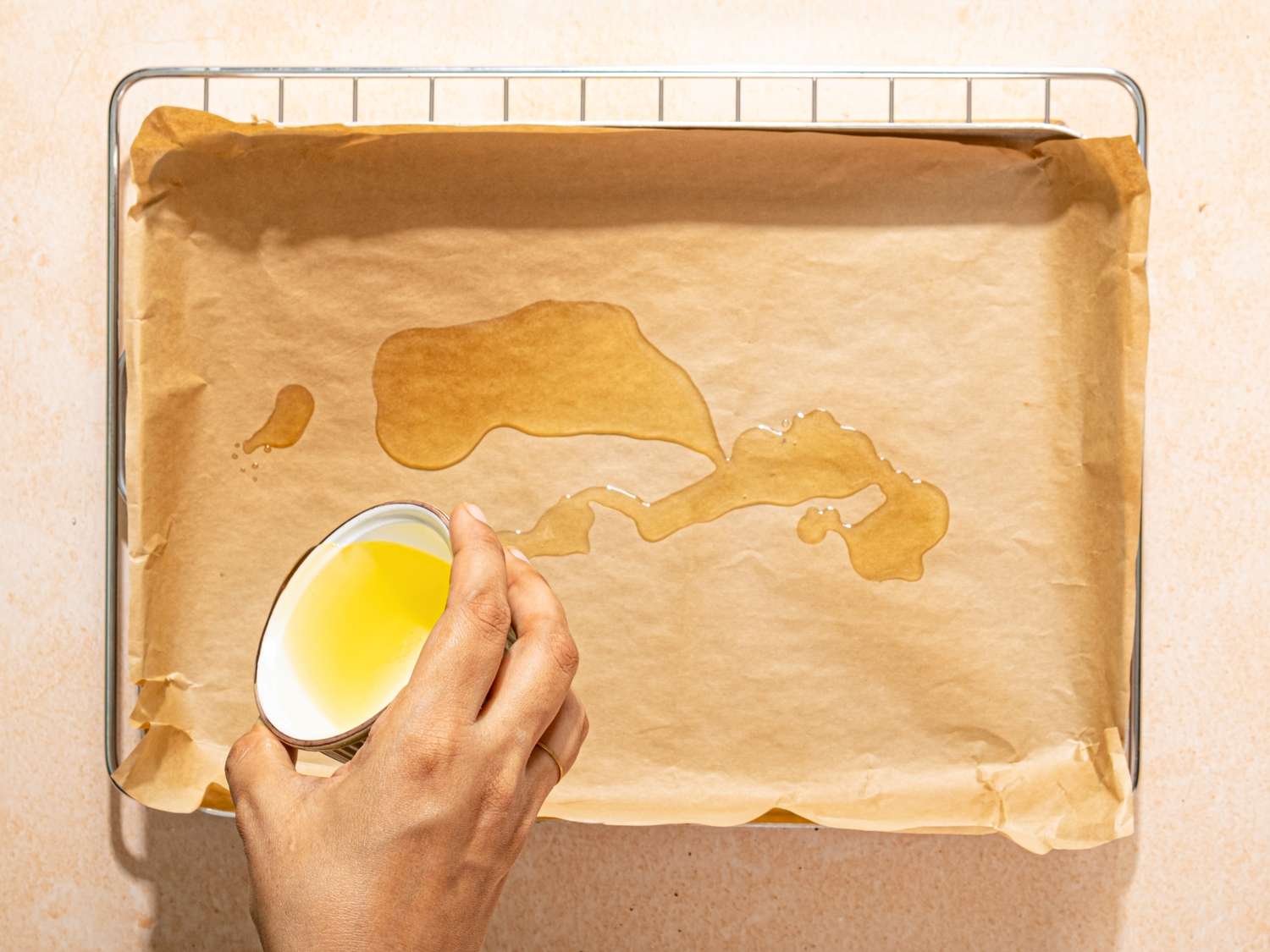 A hand pouring oil onto parchment paper on a baking tray