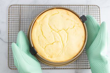 A person placing a springform pan onto a cooling rack