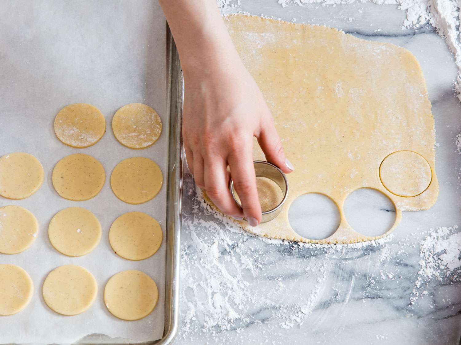 Author uses a round cutter to make circles of rolled-out dough. The circles are placed on a parchment-lined baking sheet.