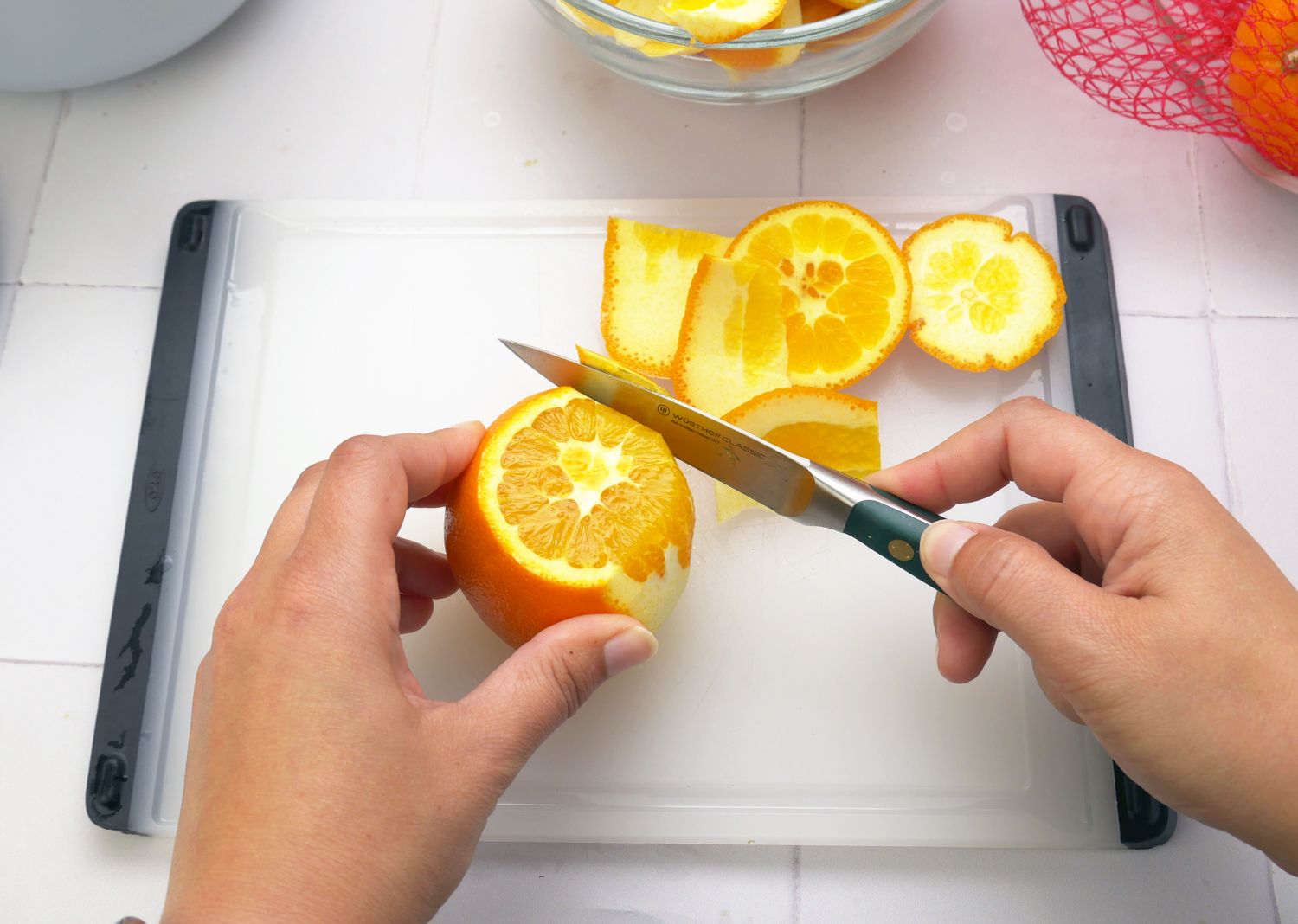 a person using a paring knife to peel an orange