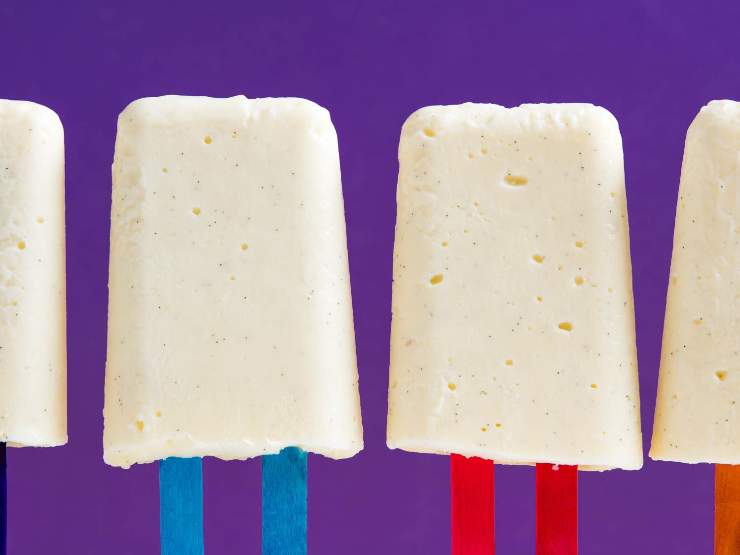 Closeup of several uncoated vanilla pudding pops on a purple background.