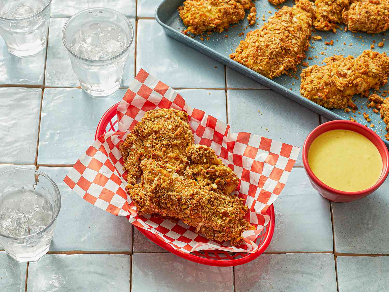 Honey mustard chicken tenders in a basket with dip, more tenders on a tray in the background.