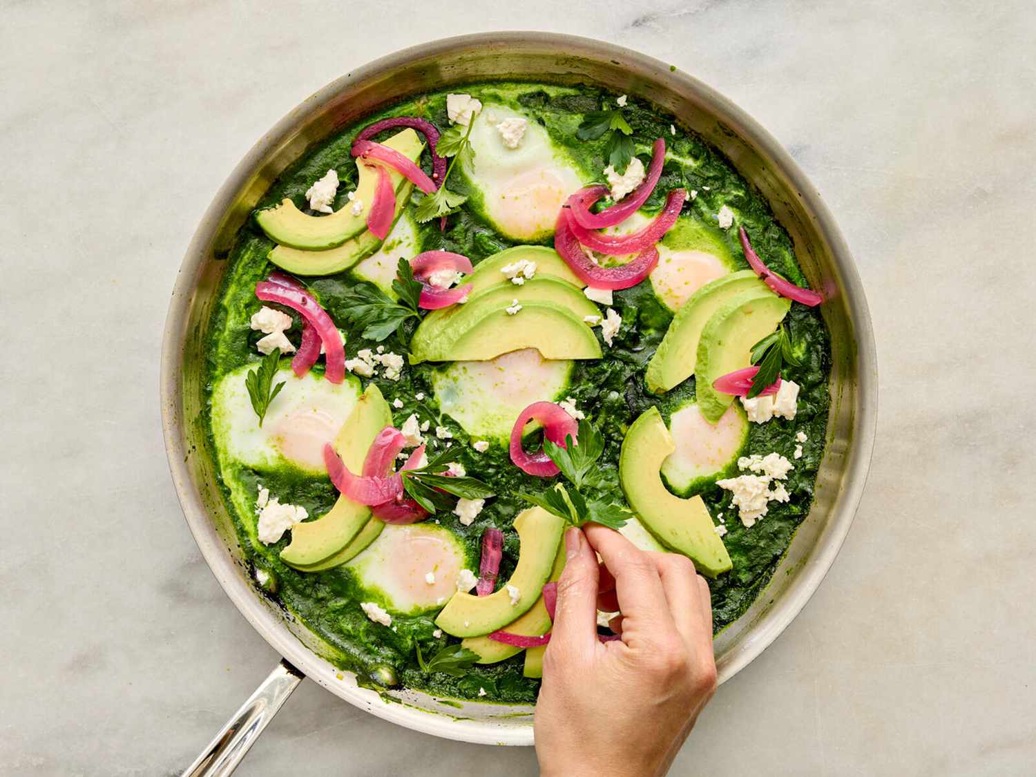 Topping shakshuka with feta, avocado and picked onion in a skillet