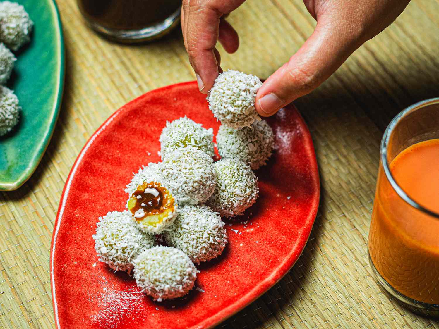 Overhead view of a hand picking up an onde-onde from a platter full with one cut open to see the inside 