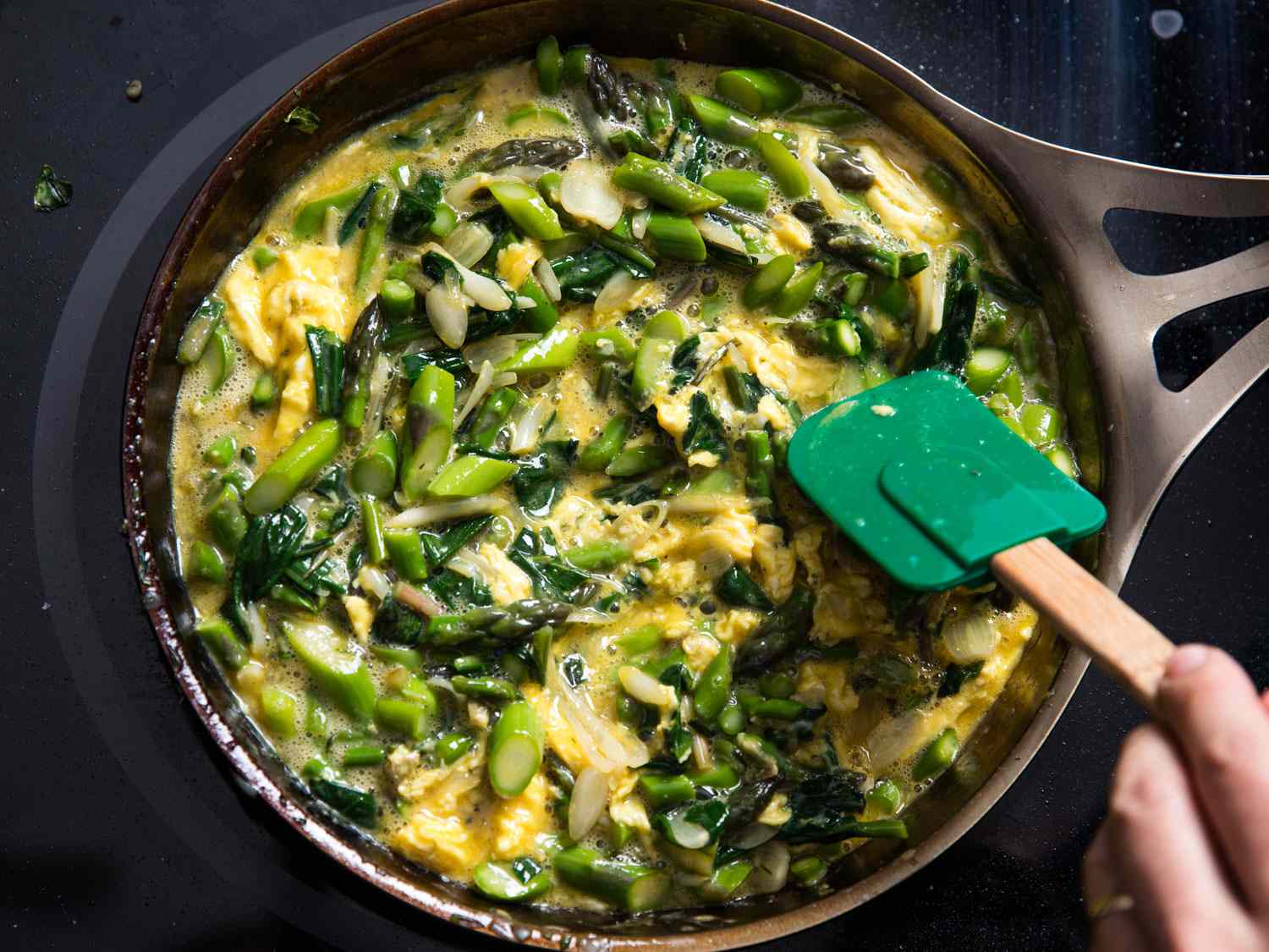 A not-yet-set ramp and asparagus omelette being gently pushed with a silicone spatula.