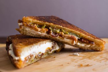 A grilled jalapeño popper cheese sandwich, cut in half on the diagonal and shingled on a cutting board.