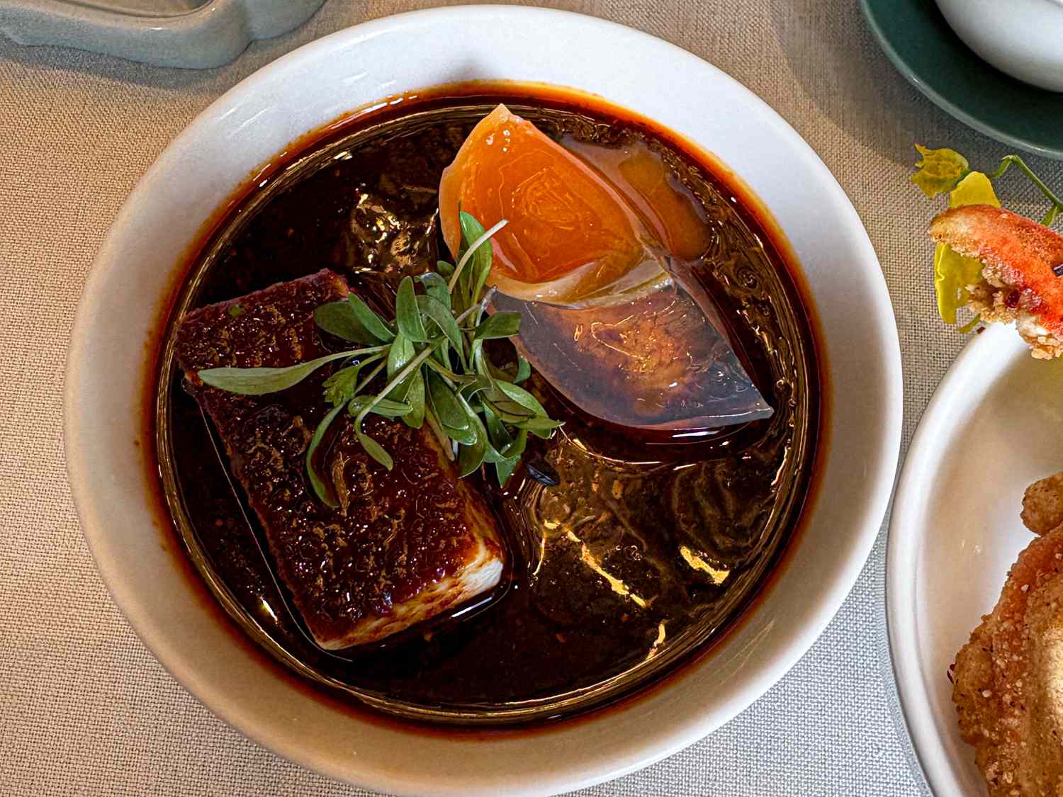 A bowl of soup with tofu herbs and a colorful garnish