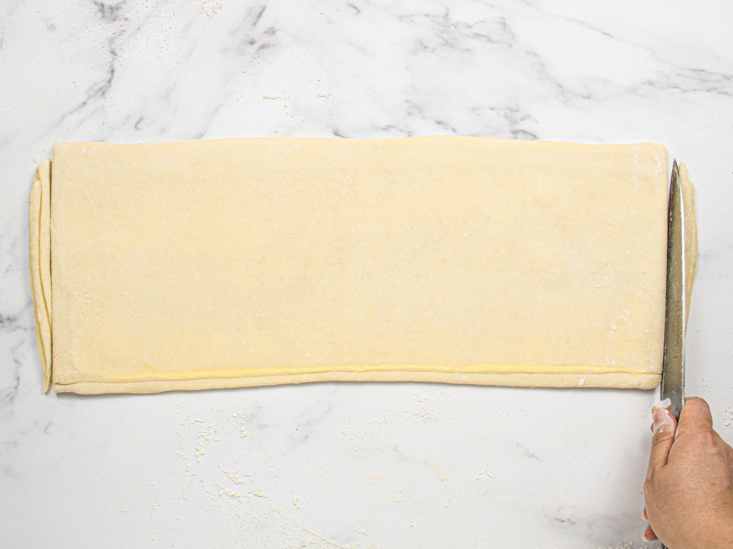 A person cutting folded croissant dough on a surface using a knife