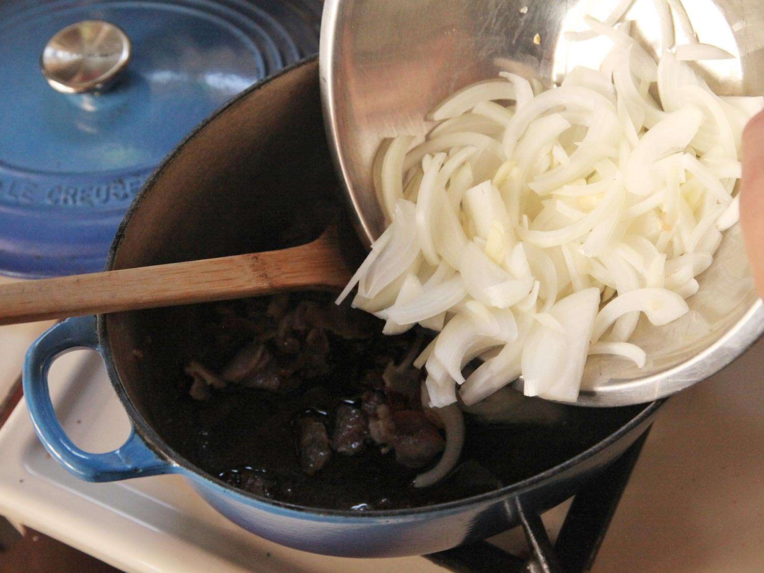 Adding sliced raw onions to bacon in Dutch oven