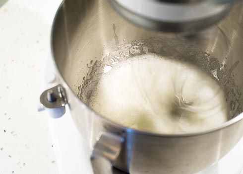 Egg whites being whipped in a mixing bowl until frothy. 