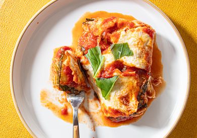 A plate with a zucchini parmesan dish garnished with basil accompanied by a fork