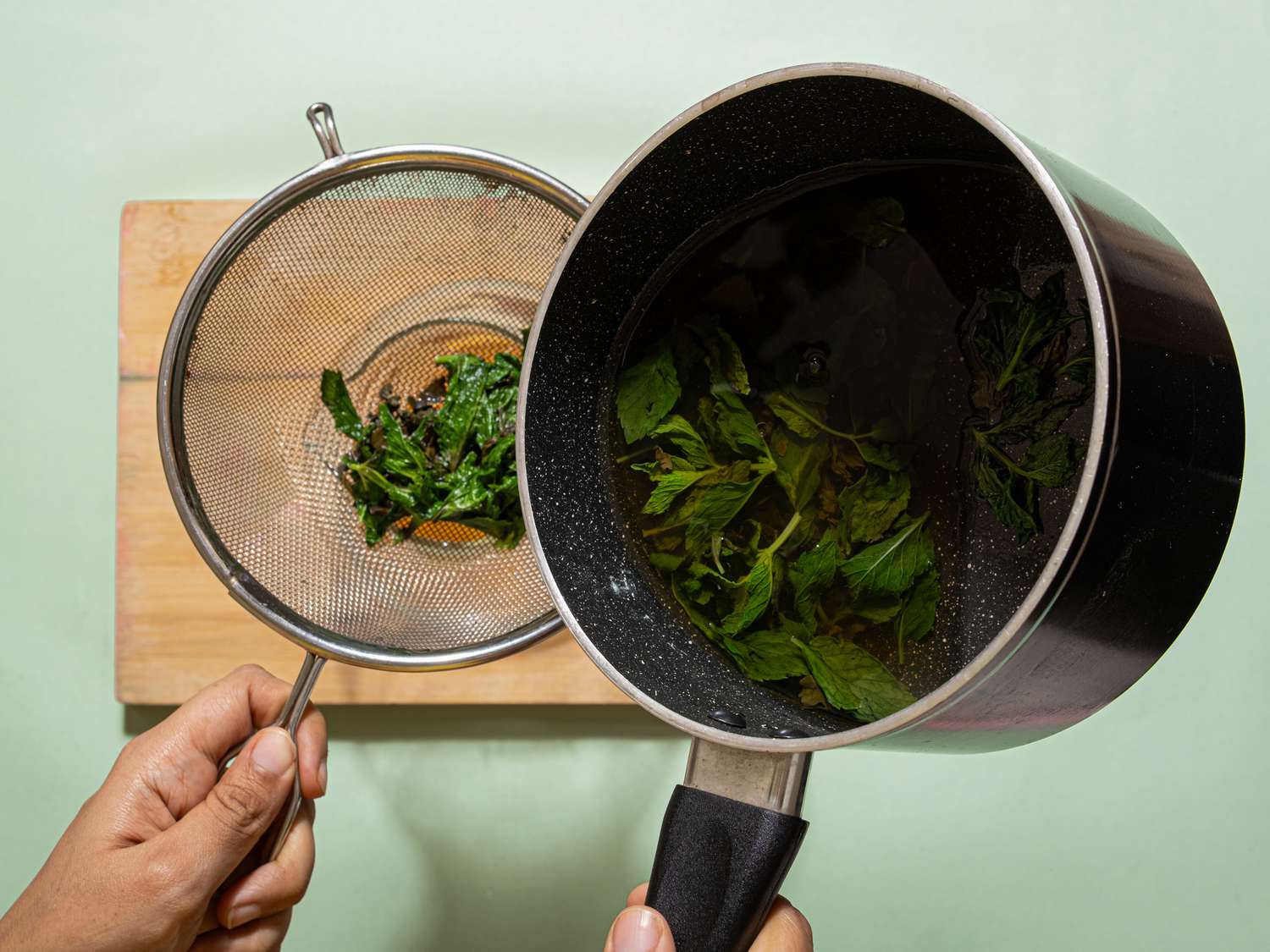 Pouring infused mint leaves through a strainer into a bowl