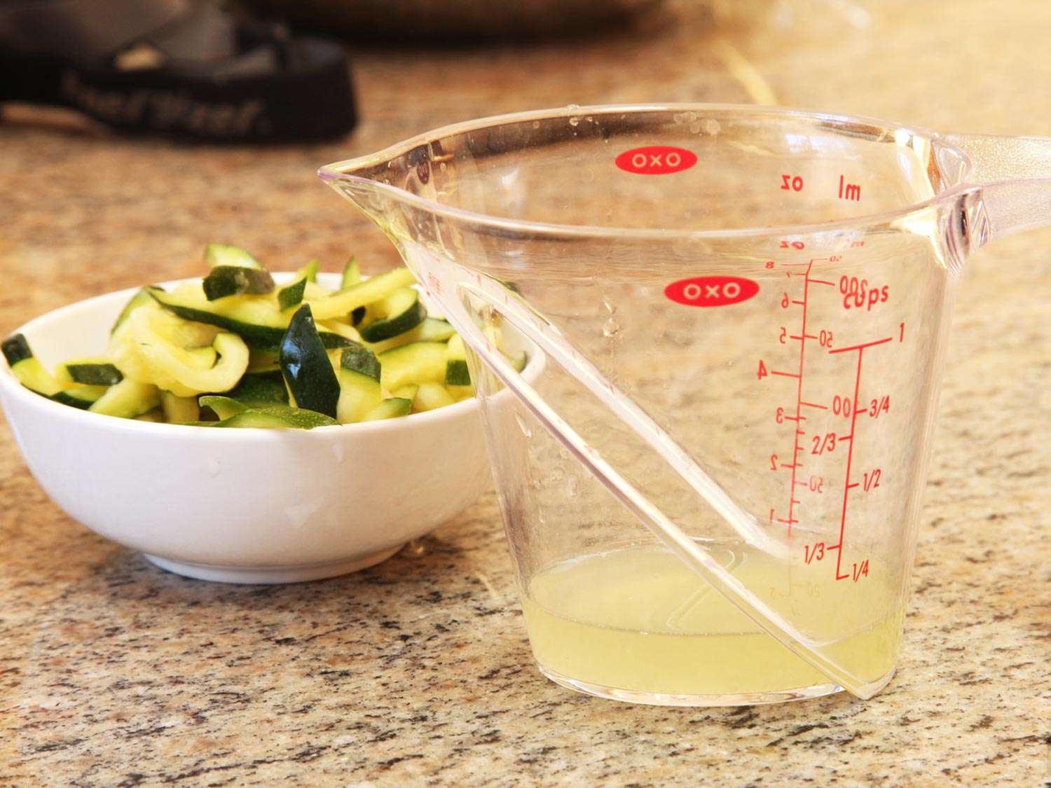 Purged zucchini water in a 1-cup liquid measure. The salted and squeezed zucchini matchsticks are in a bowl nearby.