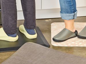 A closeup of two people's feet in kitchen clogs standing on anti-fatigue mats