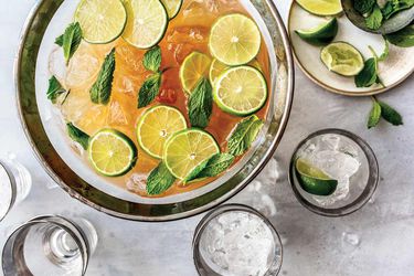 Overhead view of a punchbowl full of L'Aventura Punch, garnished with lime wheels and mint leaves.