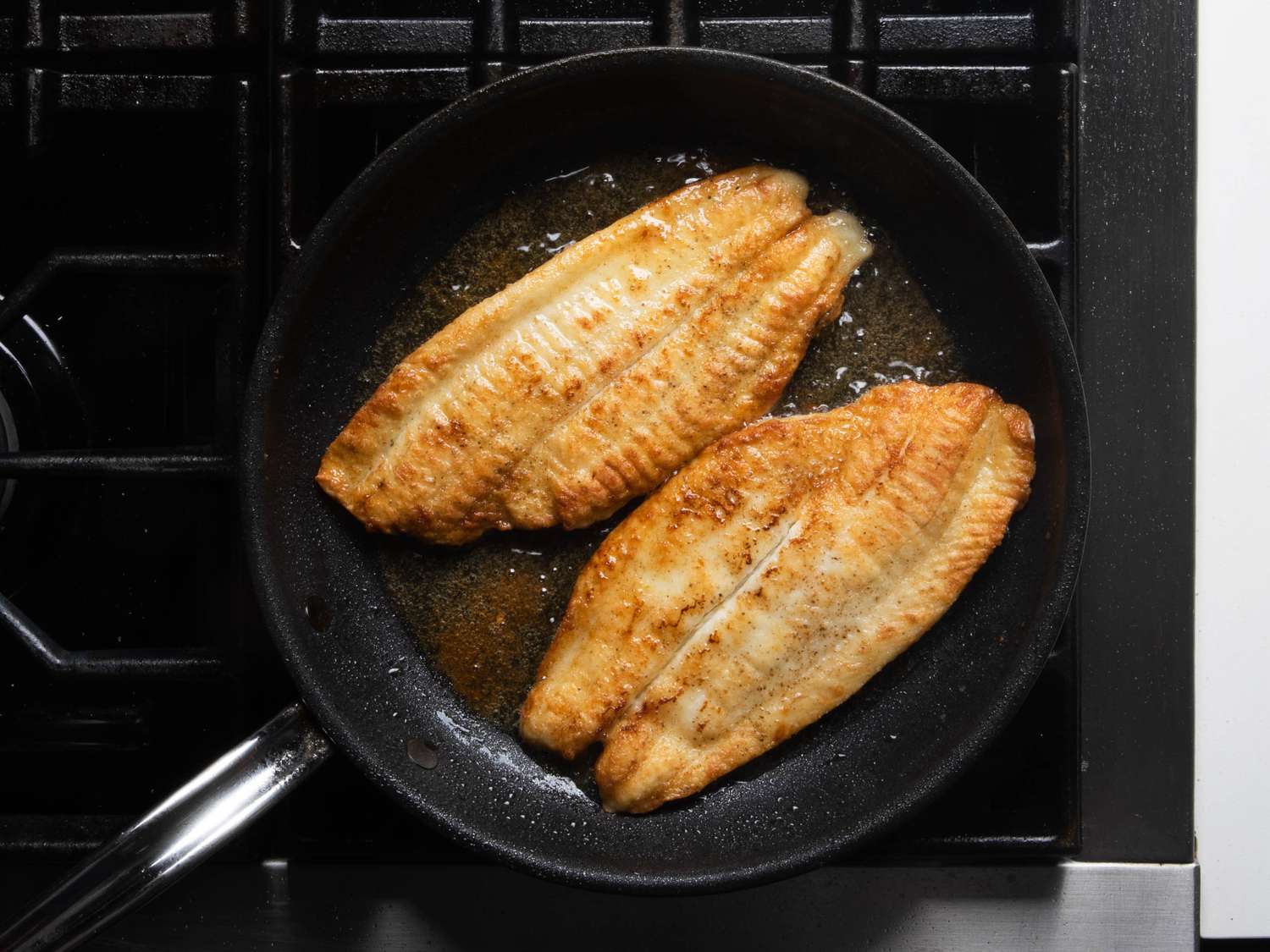 Two well-browned fish fillets sit in the skillet, having just been flipped over.
