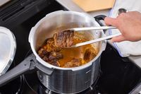 A person removes cooked meat from the IMUSA 7 Quart Stovetop Aluminum Pressure Cooker