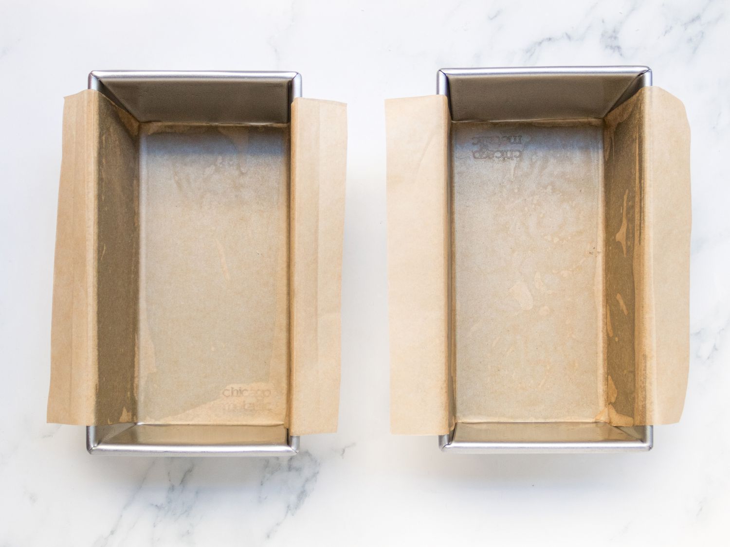 Two 9x5 inch loaf pans lines with parchment paper with wings hanging over the edges 