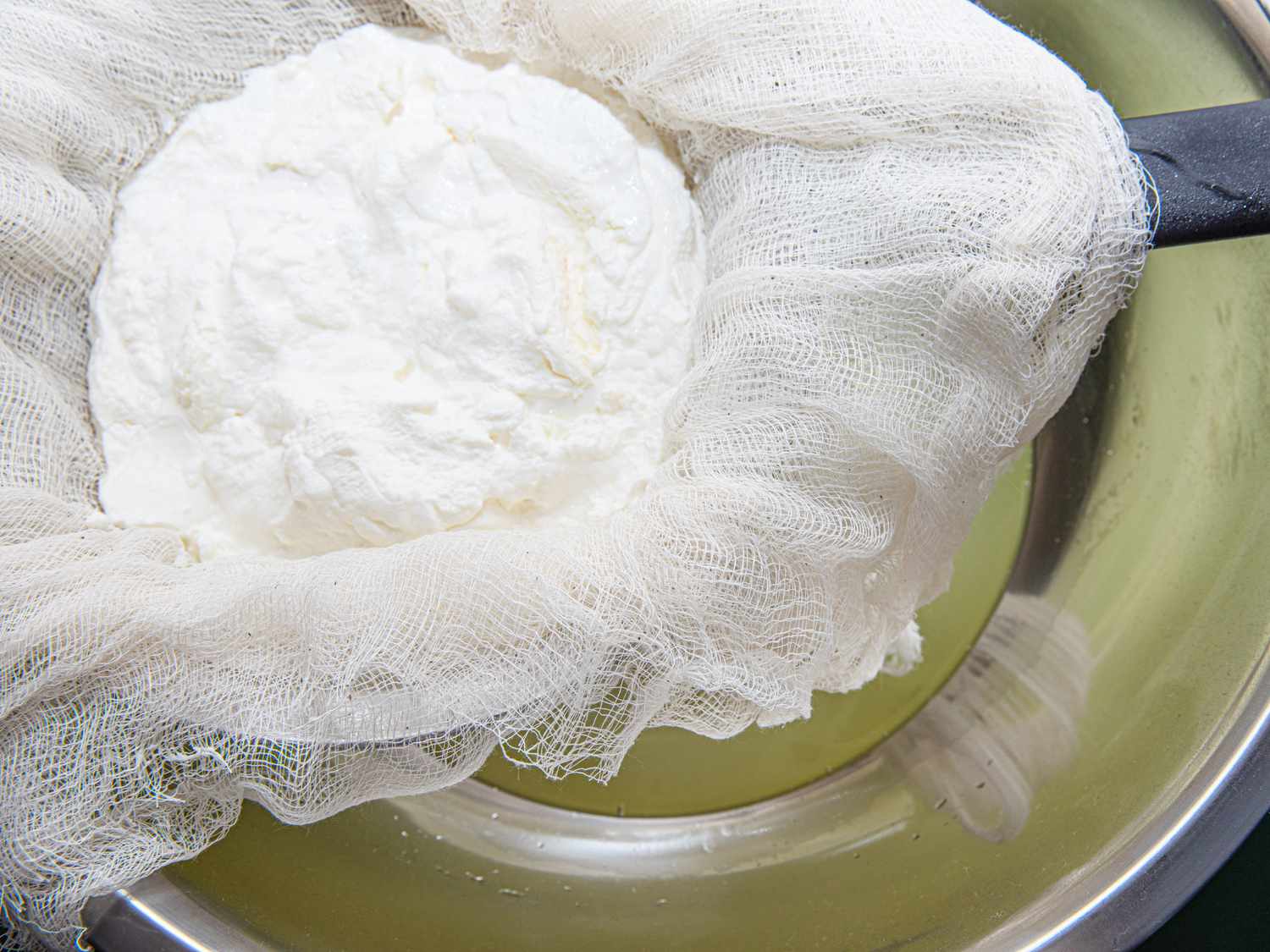 Strained labaneh sitting over a bowl with the whey that was drained from it