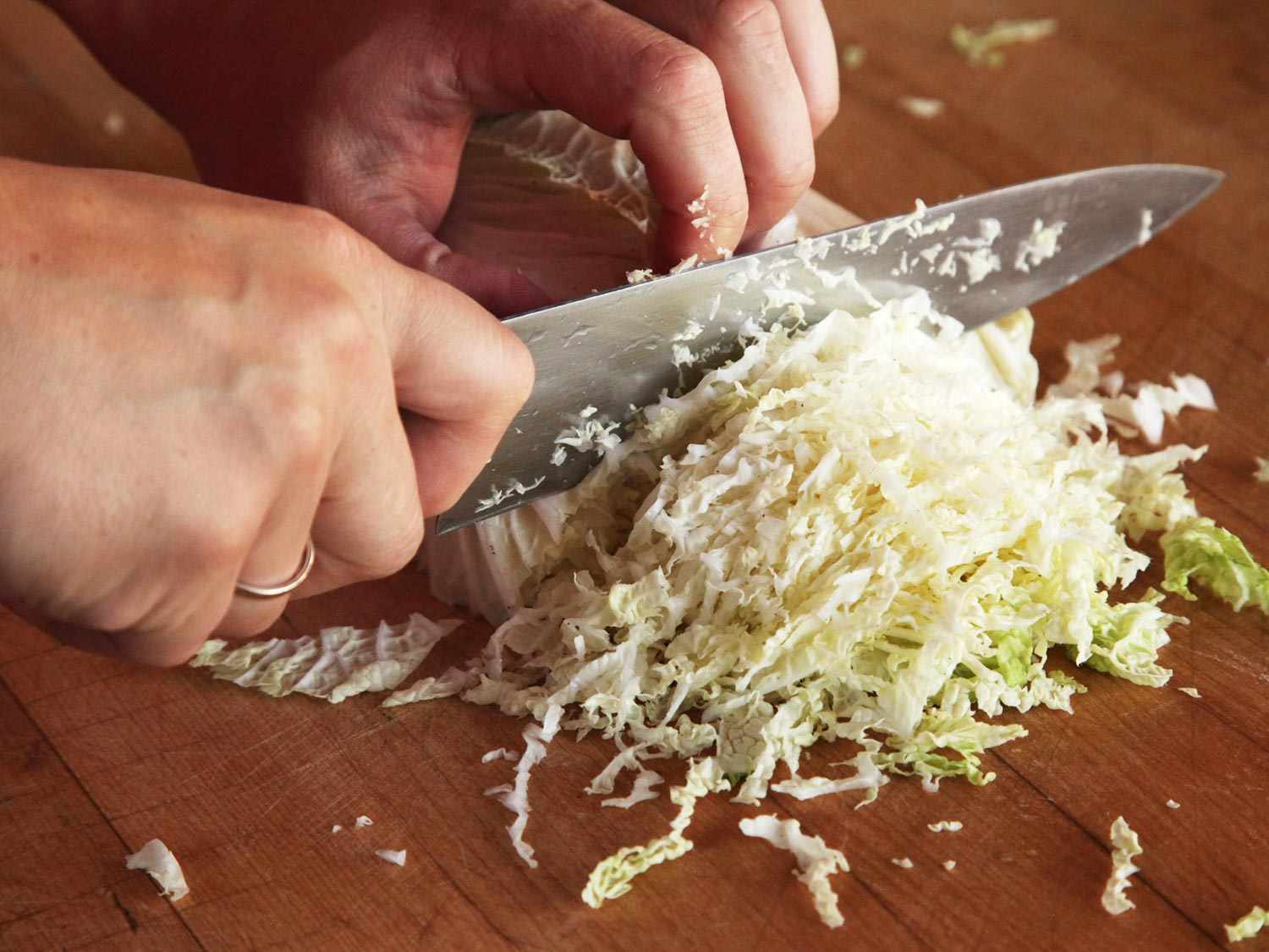 Finely shredding napa cabbage with a knife on a wood cutting board. 