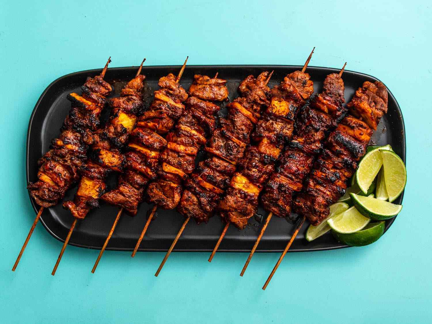 Overhead shot of grilled al pastor skewers on a serving platter with lime wedges.