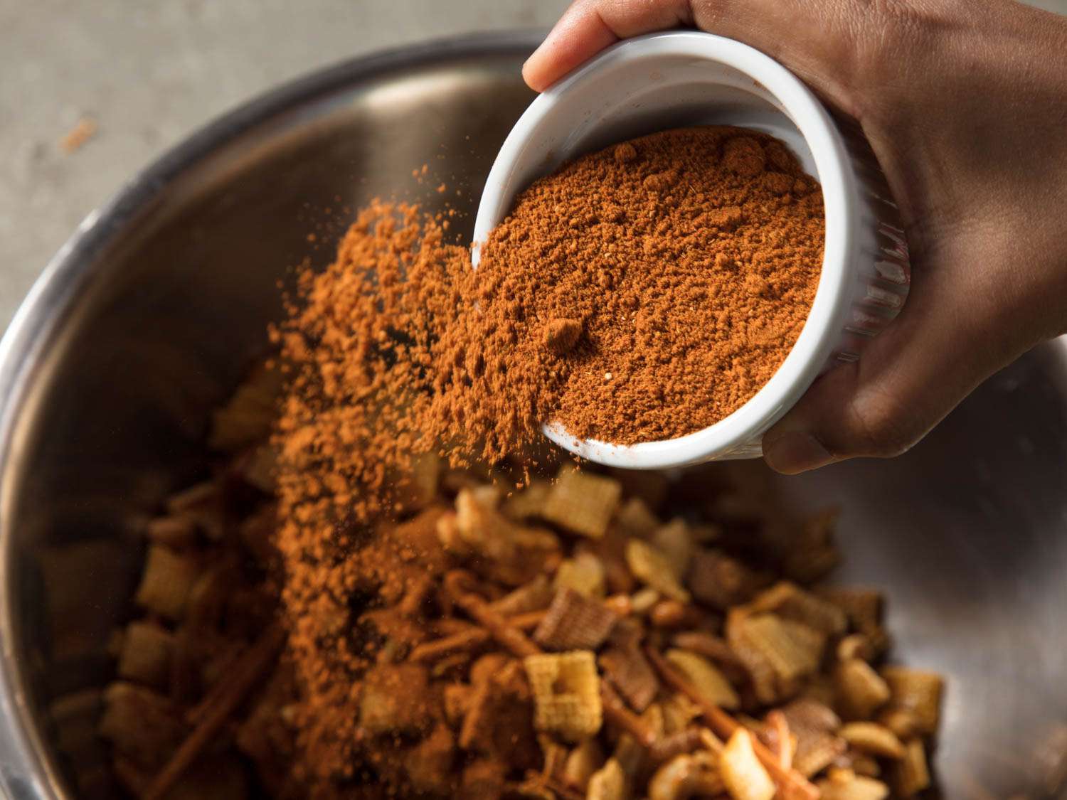 Chaat masala being tossed over the bowl of chex mix.