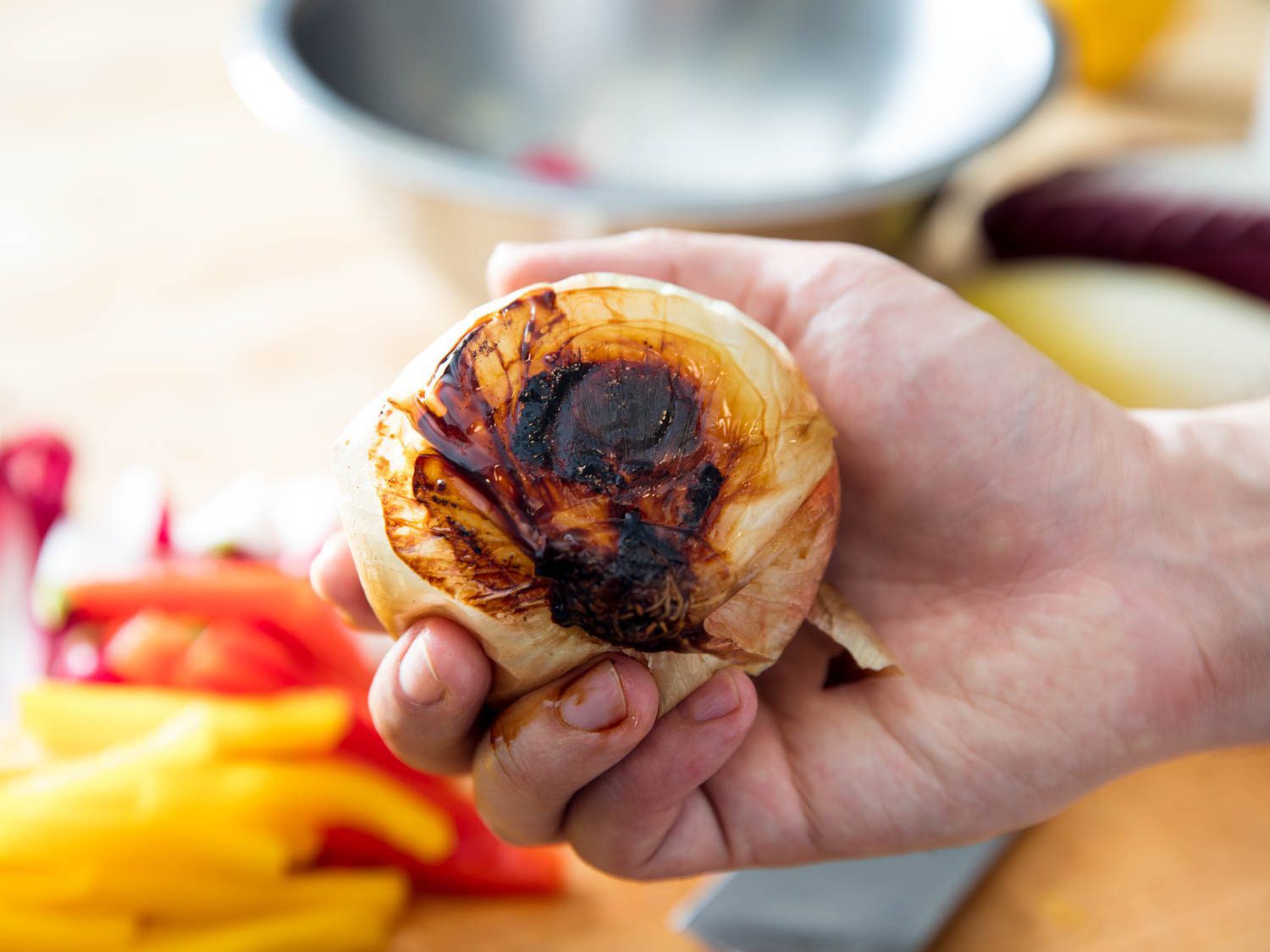 A hand holding a whole roasted, charred onion.