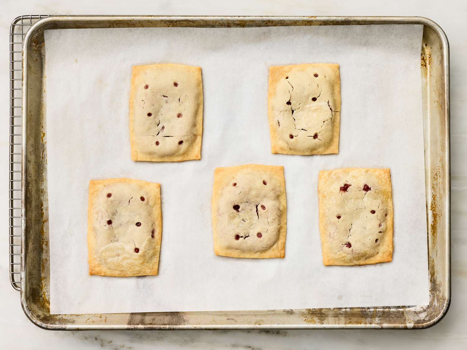 Five rectangular pastries with fruit filling, arranged on a baking sheet lined with parchment paper