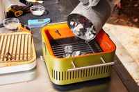 Bin pouring charcoal into the Everdure Cube Portable Charcoal Grill 