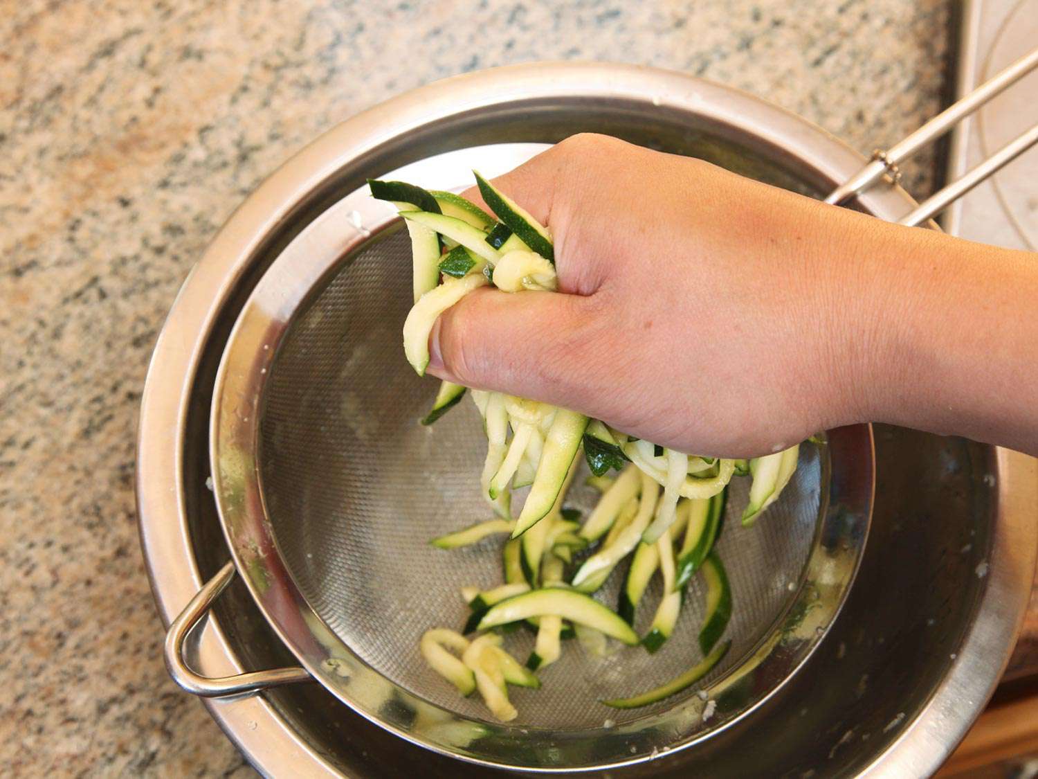 Author squeezes salted zucchini over a fine-mesh strainer nested in a mixing bowl.