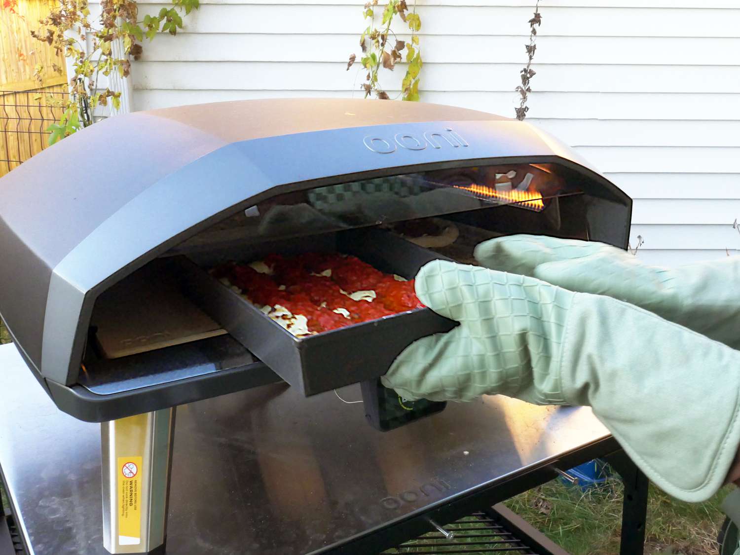 a person sliding a detroit pizza into the ooni koda 2 max 