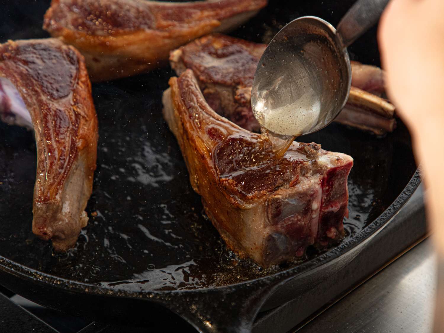 Lamb chops being basted with sauce in a cast iron skillet
