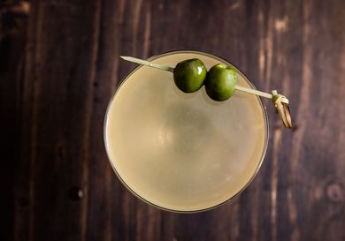 Overhead shot of a mezcal dirty martini with two skewered olive perched on the rim