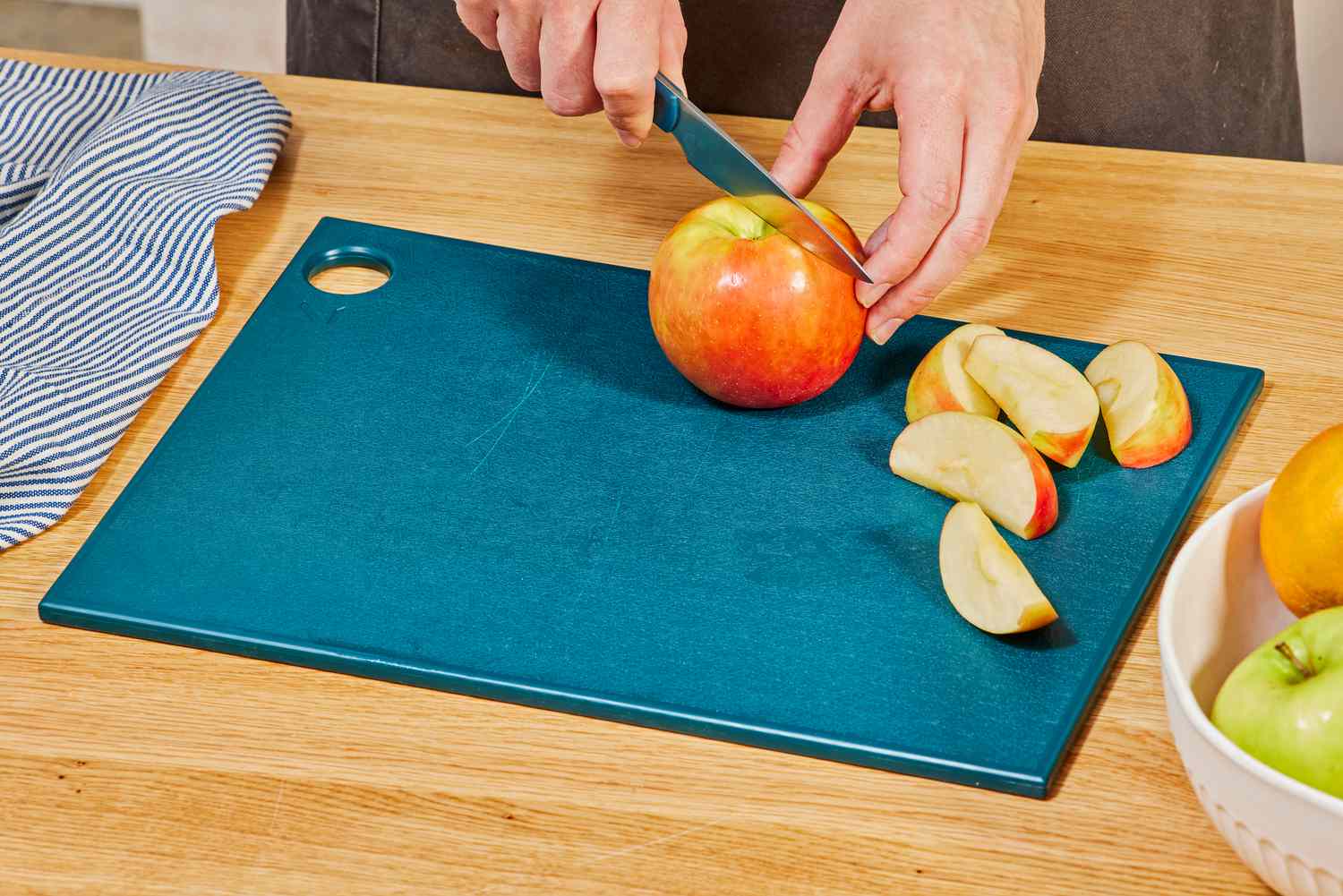 A person cutting an apple on a plastic cutting board