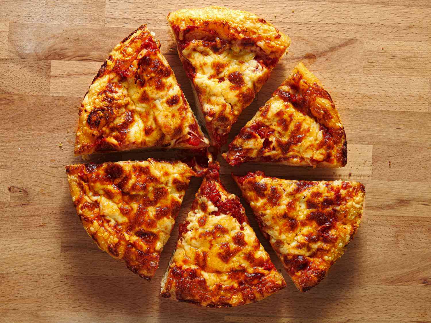 The pizza, cut into size slices, on a wooden cutting board.