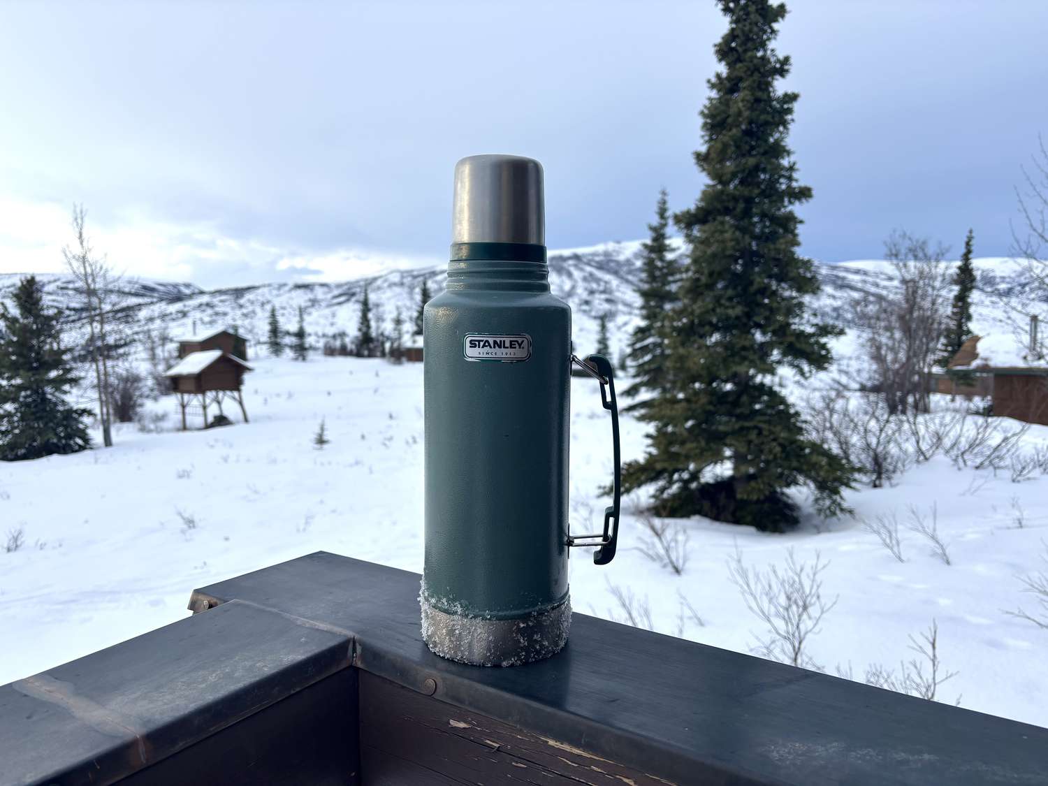 A Stanley thermos sitting on the ledge of a porch balcony.