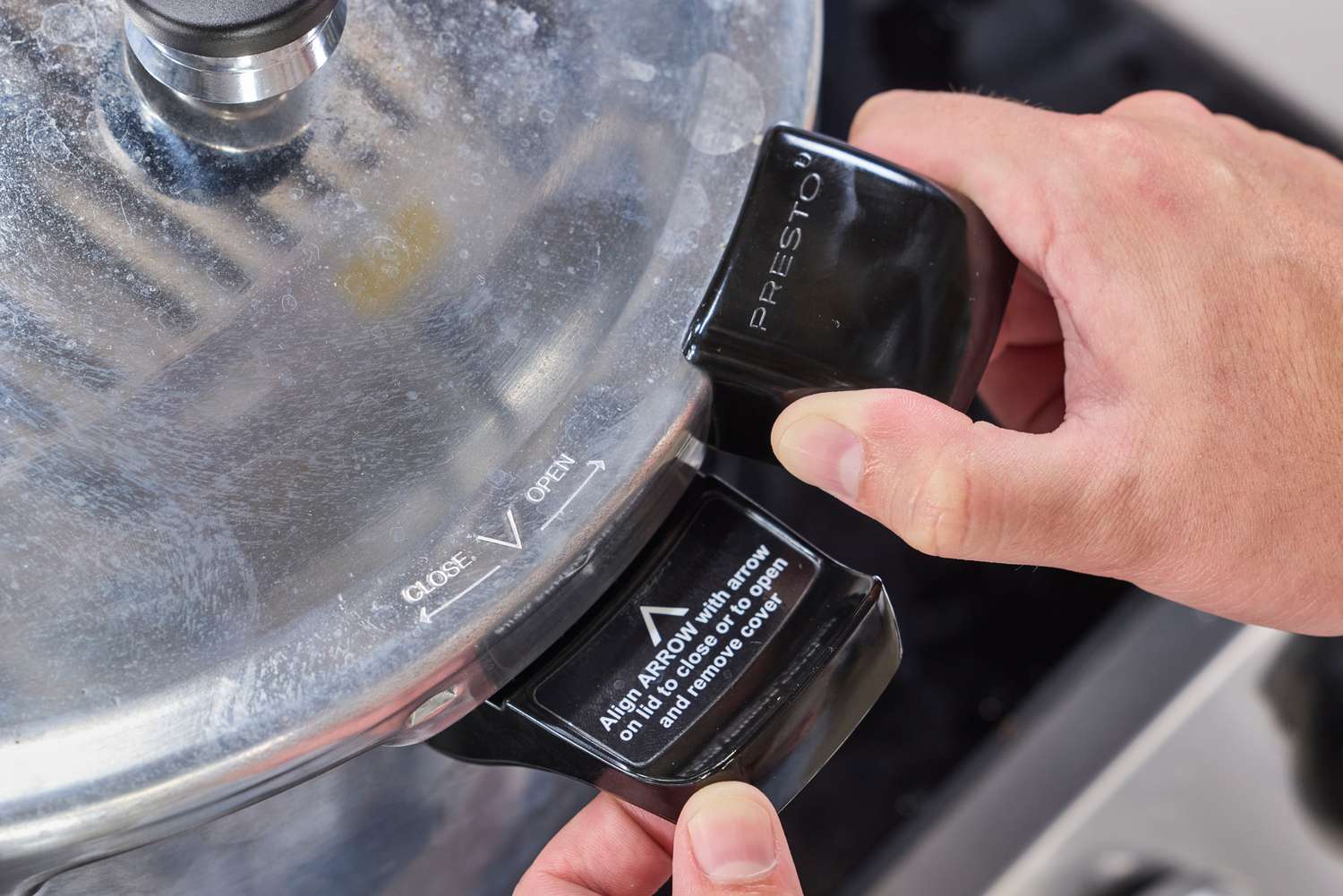 A person holding the handle of the Presto 16-Quart Pressure Canner and Cooker lid