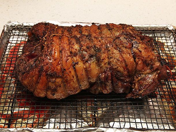 Cooked lamb roast resting on a wire rack on a rimmed baking sheet.