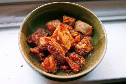 A green bowl full of cooked pork belly.