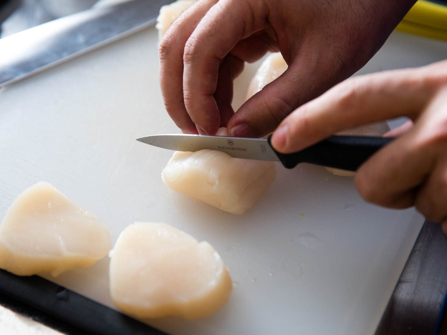 Scallops being sliced with a paring knife on a rubber cutting board.