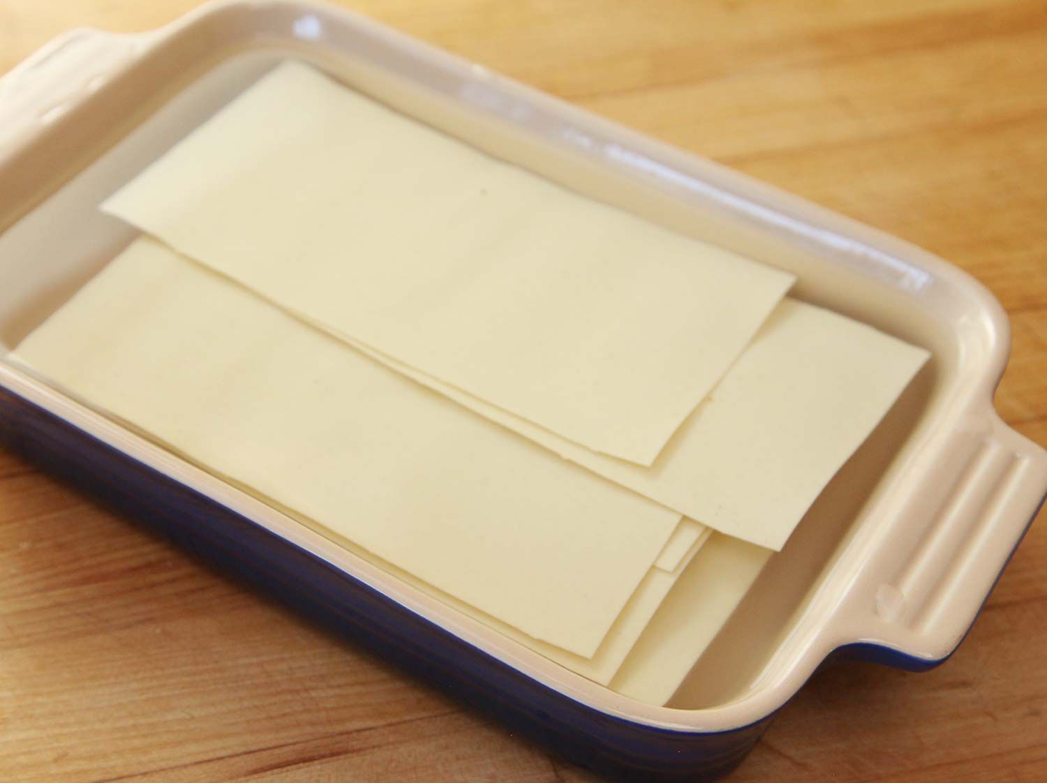 Dry pasta sheets soaking in boiling water in a casserole dish. 