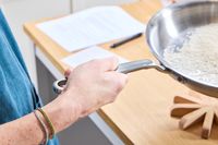 A person lifts the Made In 12-Inch Stainless Steel Skillet by the handle