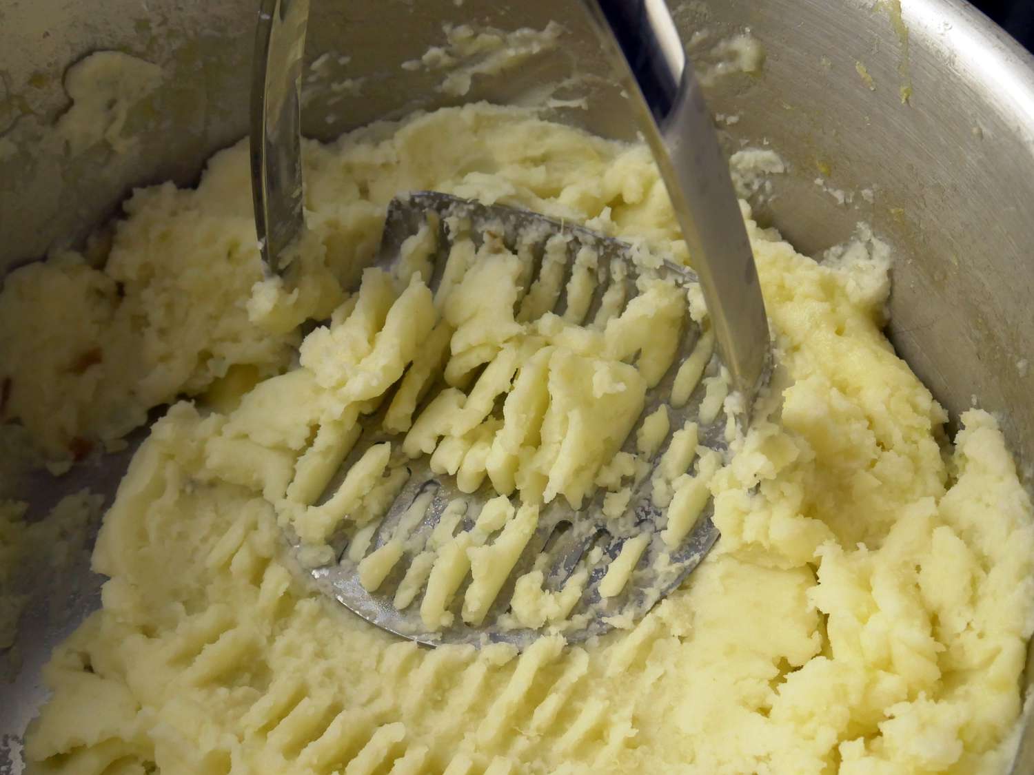 a closeup of the all-clad masher smushing potatoes in a pot