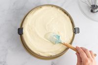 A person spreading cheesecake batter in a springform pan.