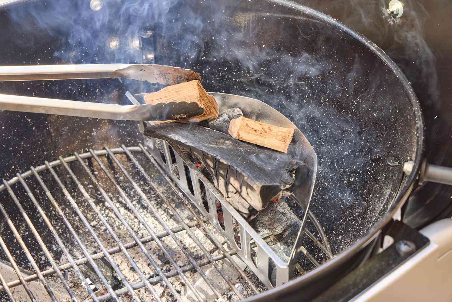 Tongs adding wood to the Weber Performer Deluxe Charcoal Grill 22-Inch