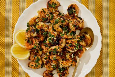 Grilled shrimp garnished with herbs next to lemon wedges on a plate