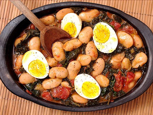 Overhead view of butter beans with kale and eggs, served in a black clay platter.