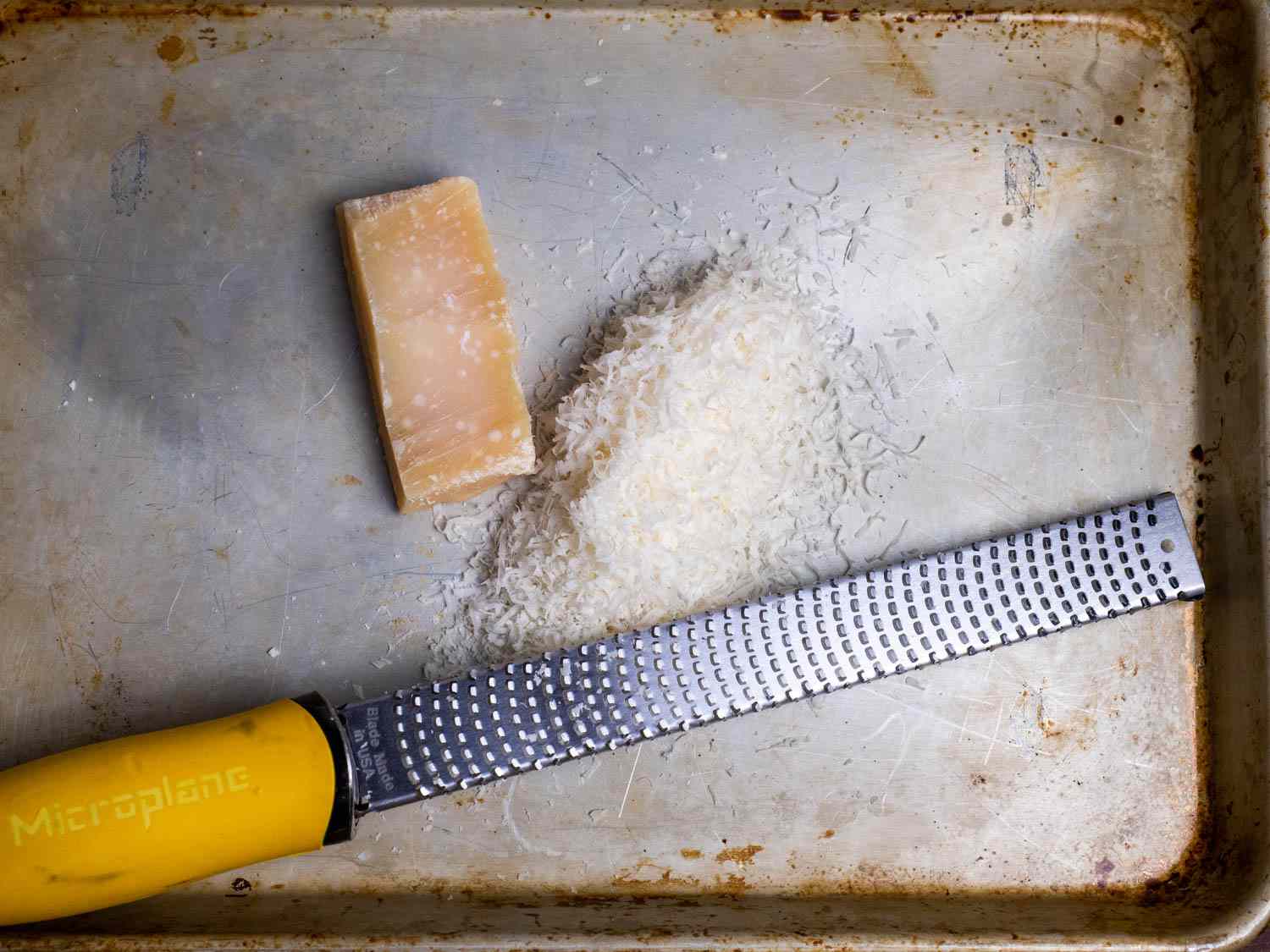 A Microplane alongside a pile of finely grated cheese and a chunk of Parmesan